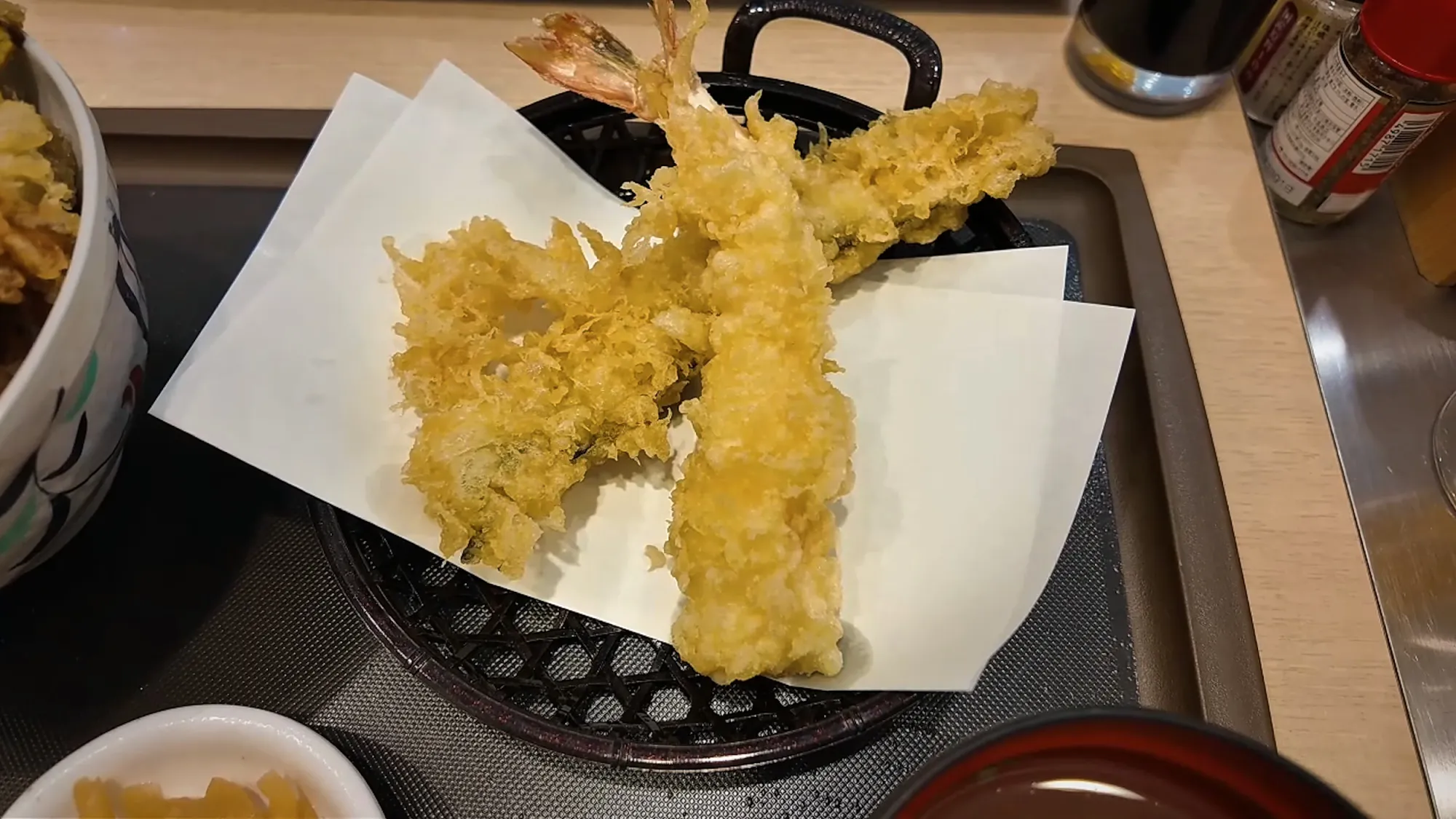 A basket of large shrimp tempura and conger eel tempura on white paper at Tendon Tenya in Tokyo.