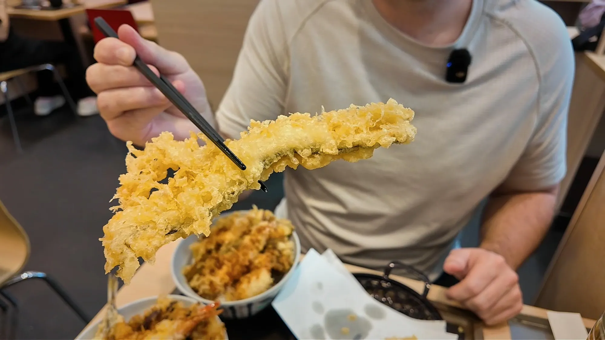 Cream lifting a long piece of shrimp tempura with chopsticks over his All-Star Tendon bowl at Tendon Tenya.