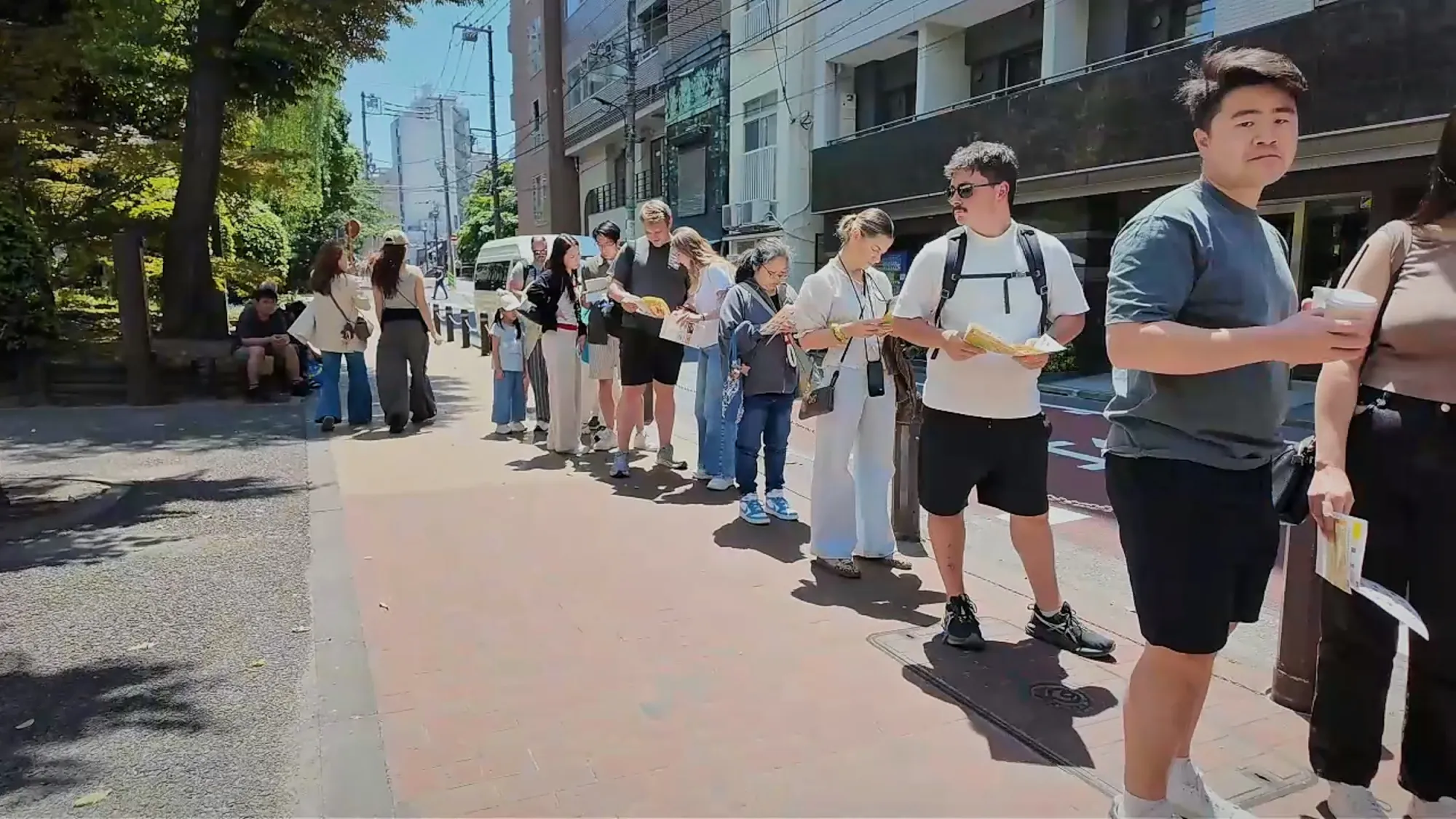 A long line of people waiting along a Tokyo sidewalk for a popular food shop.