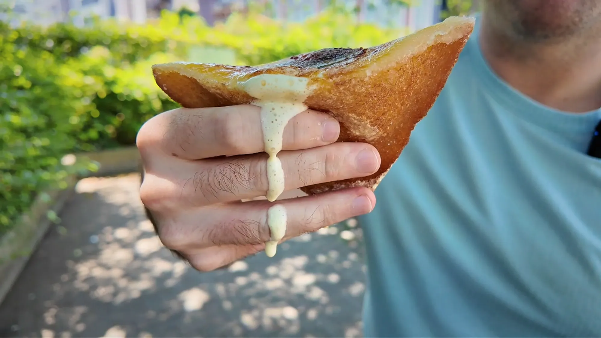 Custard dripping from a bitten crème brûlée fried sandwich held over a leafy sidewalk in Ginza.