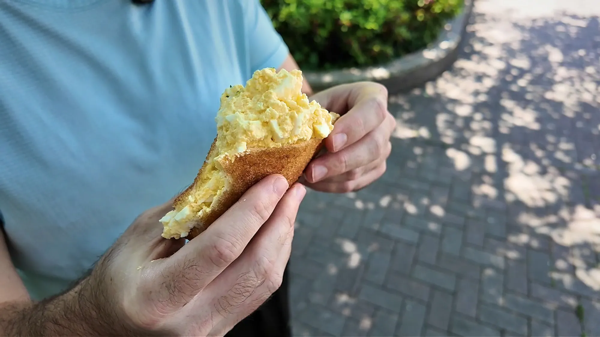 A bitten Age.3 fried sandwich with egg salad piled high out of the crispy bread, held over a sidewalk in Ginza.