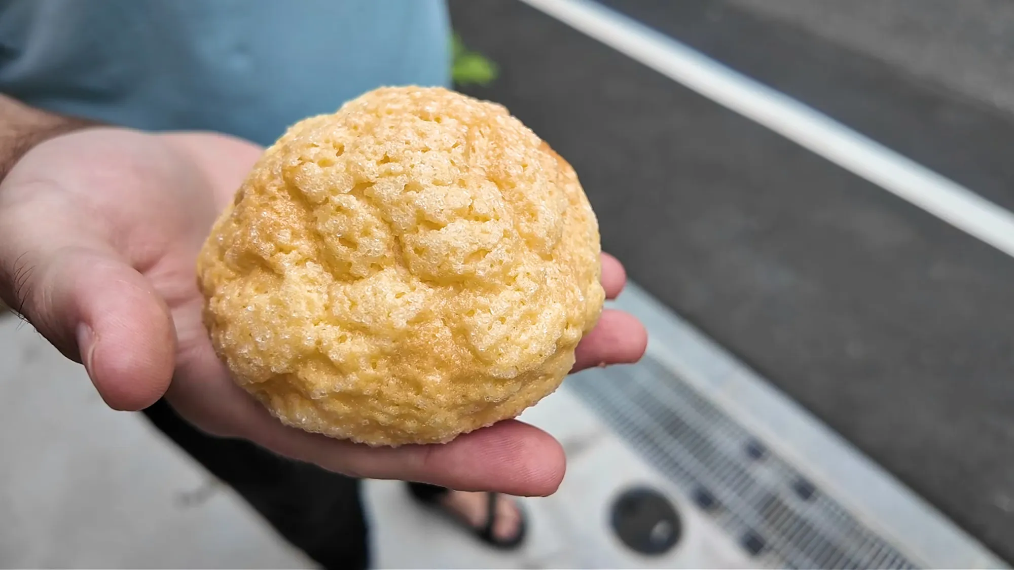 A round, sugar-crusted melon pan from a Japanese bakery in Tokyo, held in an open hand above the street