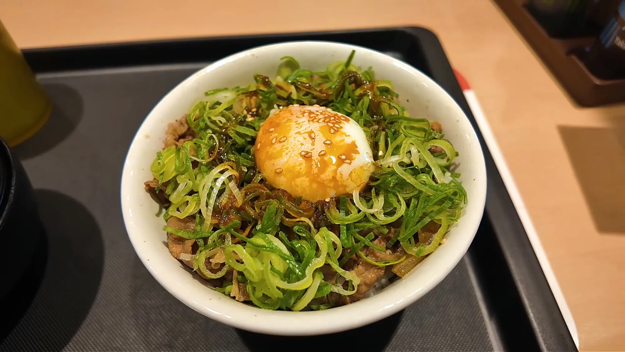 A bowl of Matsuya gyudon topped with sliced green onions and a raw egg yolk on a dark tray at Matsuya in Tokyo.