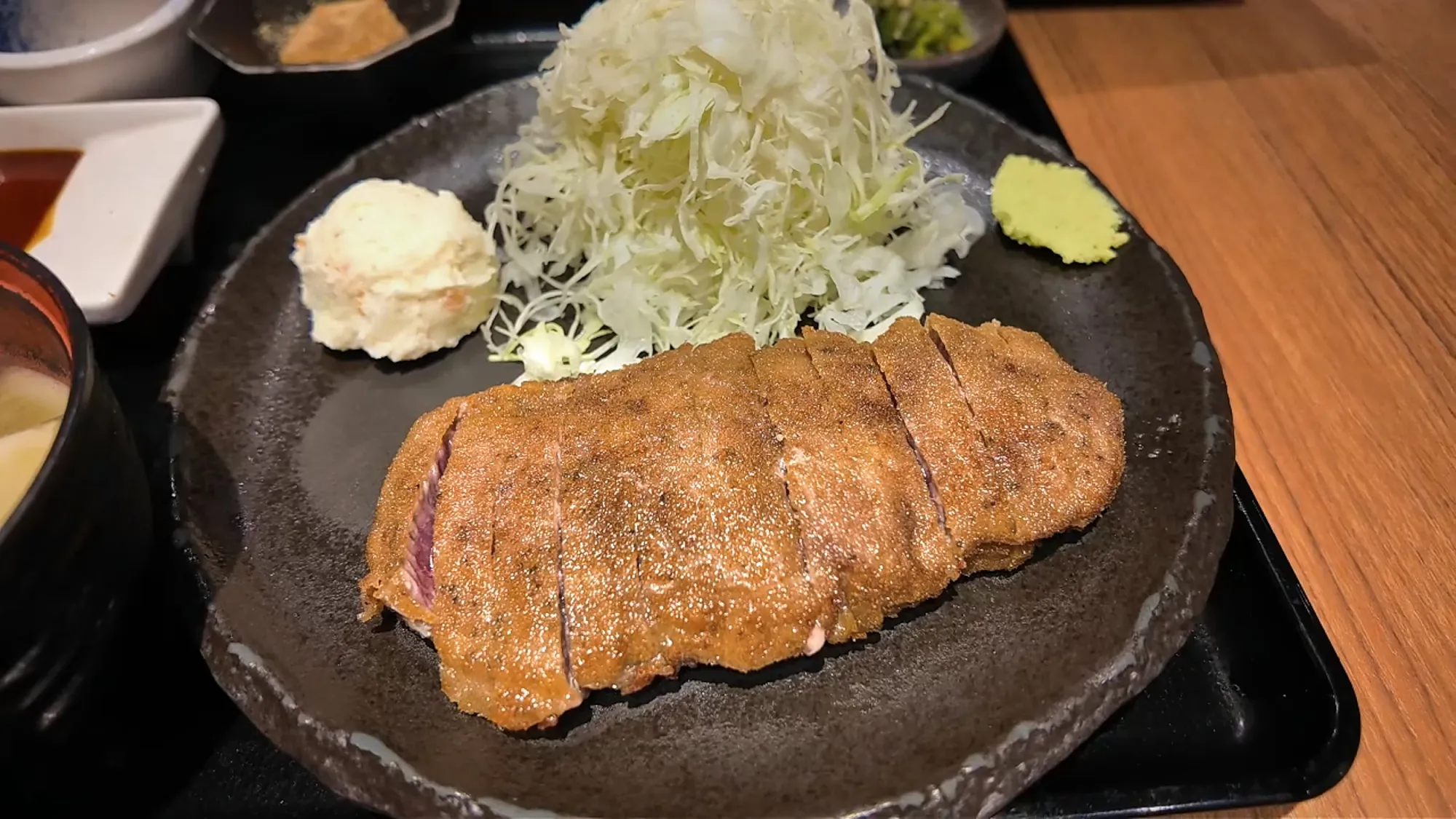 A gyukatsu beef cutlet on a black plate with shredded cabbage and wasabi at Gyukatsu Motomura