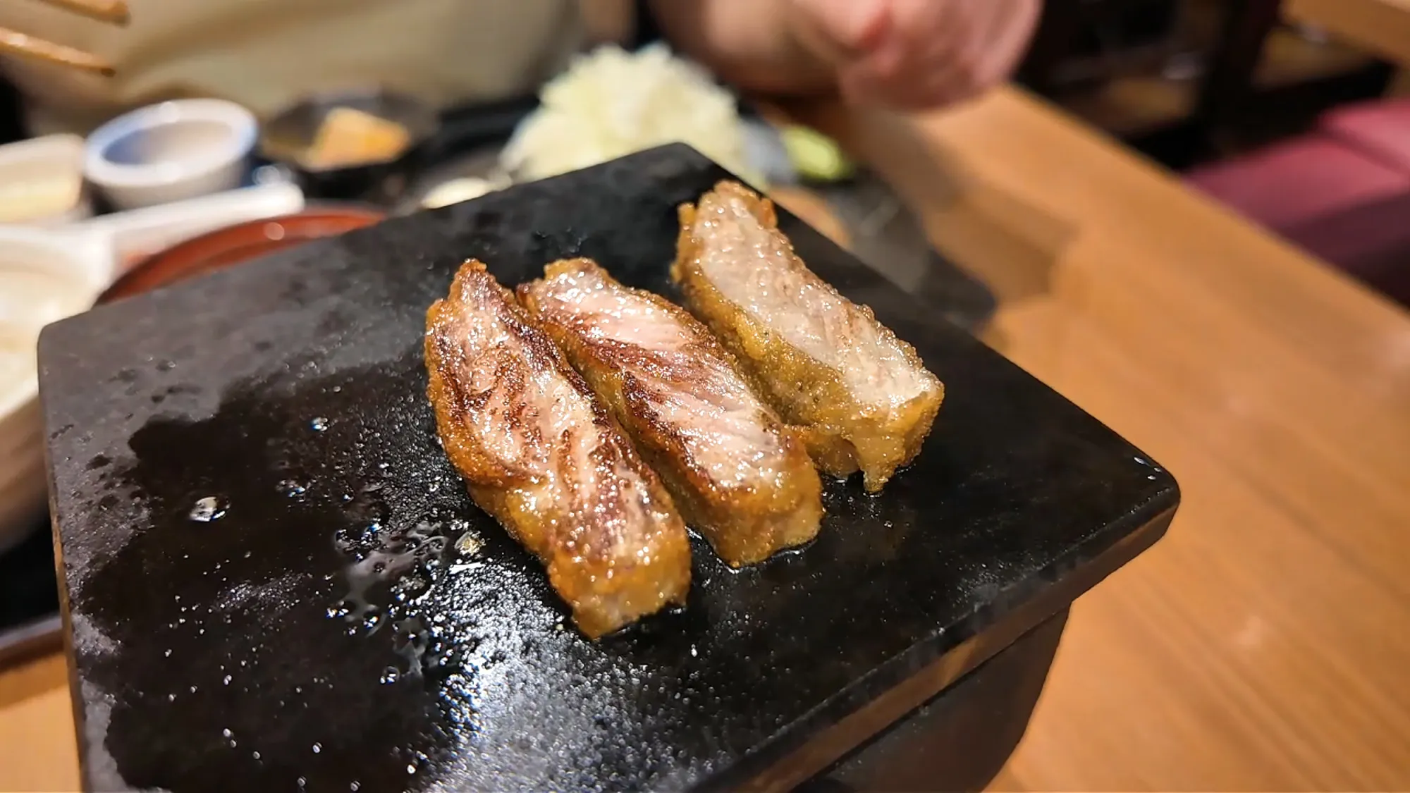 Three slices of gyukatsu seared brown on a sizzling black hot stone at Gyukatsu Motomura.