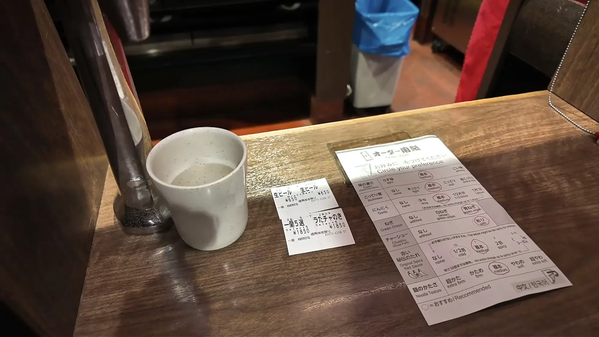 Printed Ichiran meal tickets for two ramen sets and two draft beers next to a paper order sheet and a cup of water in a booth.