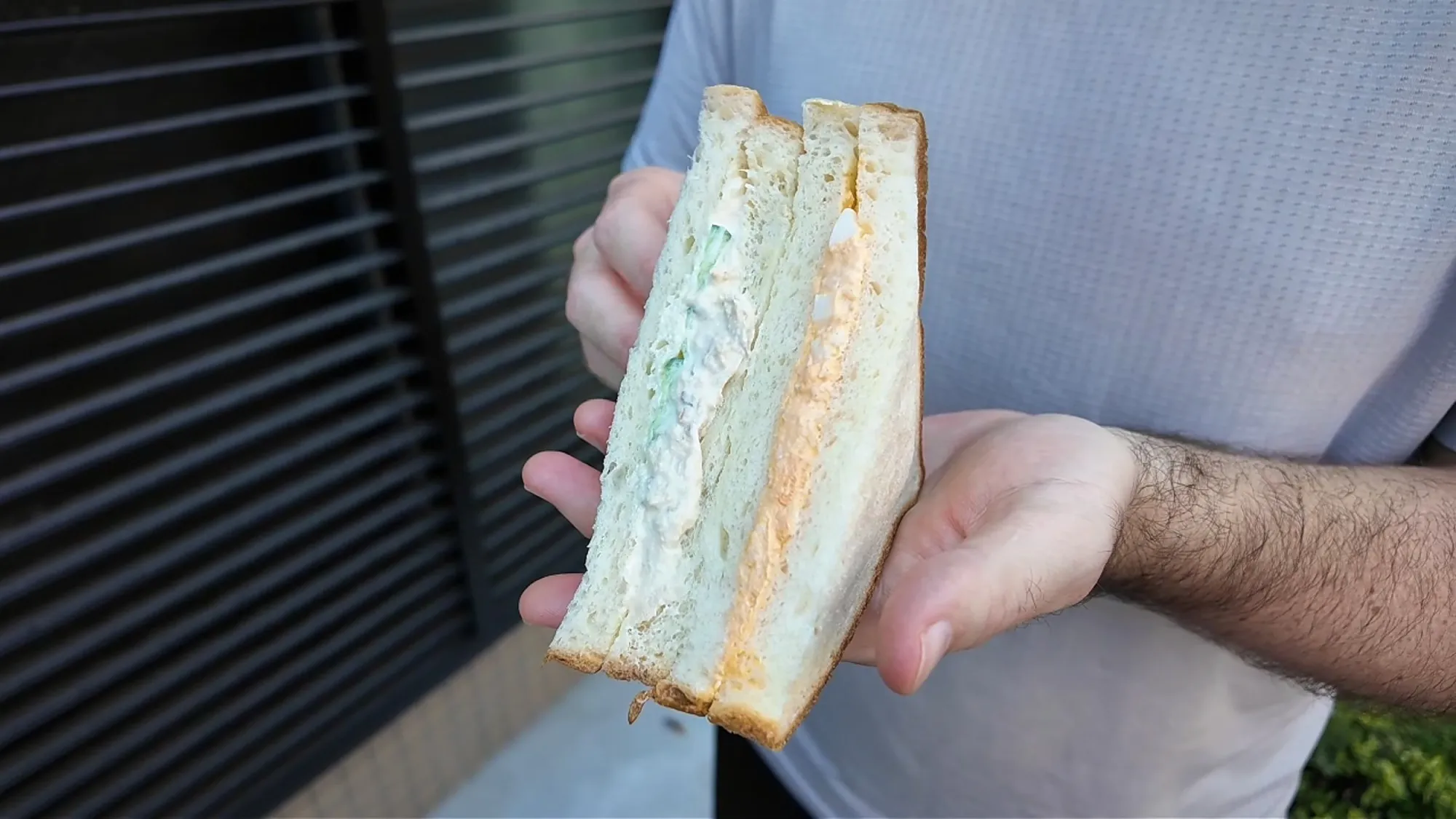 A Japanese tuna salad sandwich with cucumber and an egg salad sandwich on soft white bread, held up in one hand
