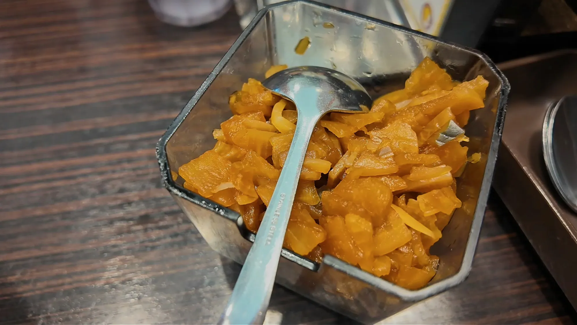 A tub of yellow pickled daikon radish with a serving spoon on a table at Yayoiken.