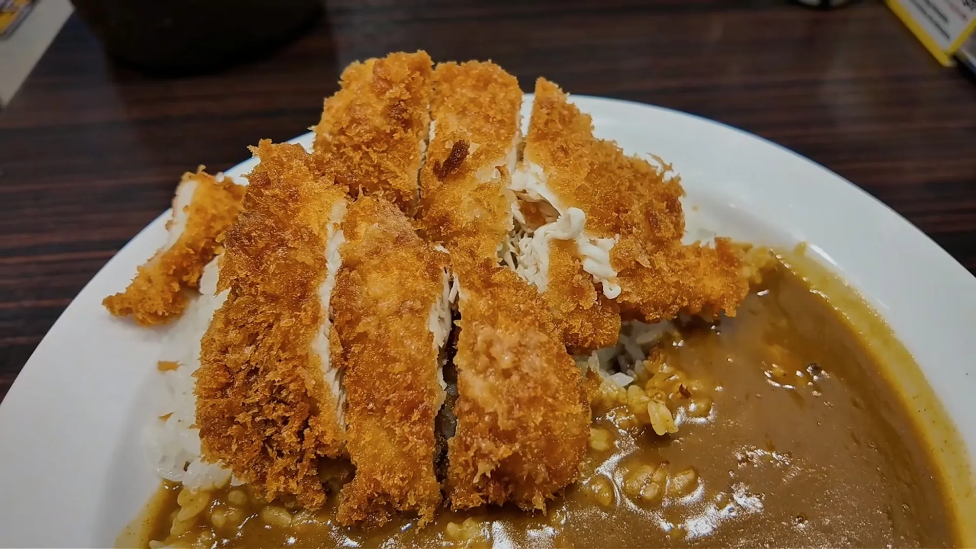 A large sliced chicken cutlet with a thick golden crust over rice and curry sauce on a CoCo Ichibanya plate in Tokyo.