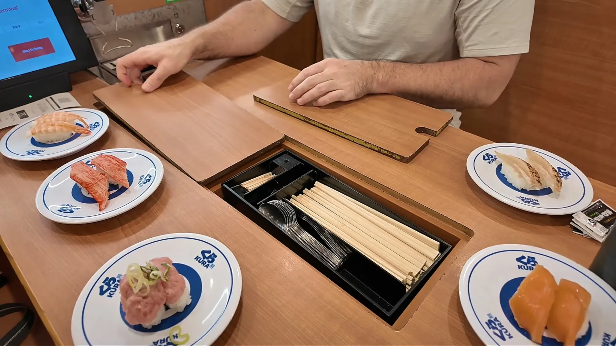 Plates of nigiri and a built-in chopstick drawer on a table at Kura Sushi in Tokyo.