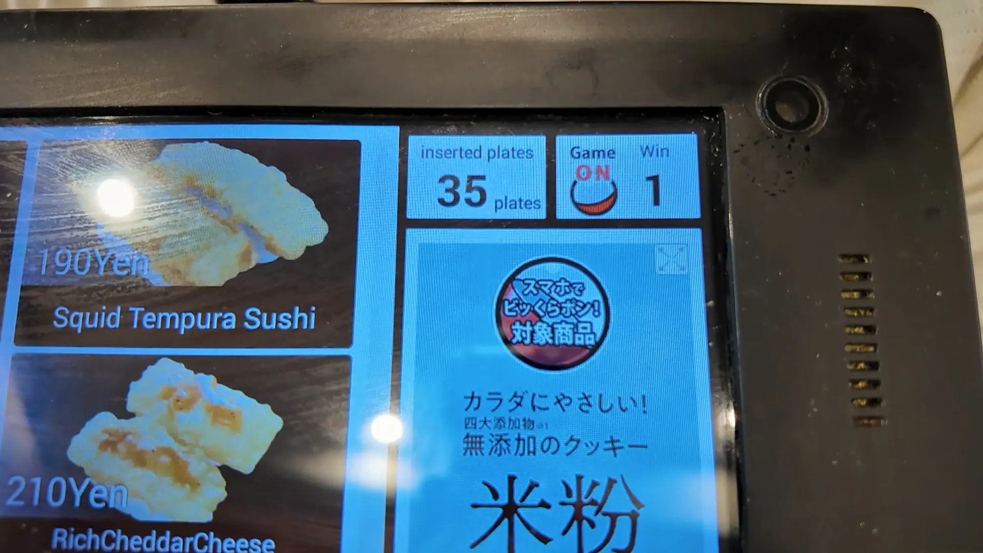 A Kura Sushi table tablet in English showing 35 inserted plates, the game switched on, and one win, next to squid tempura sushi for 190 yen.