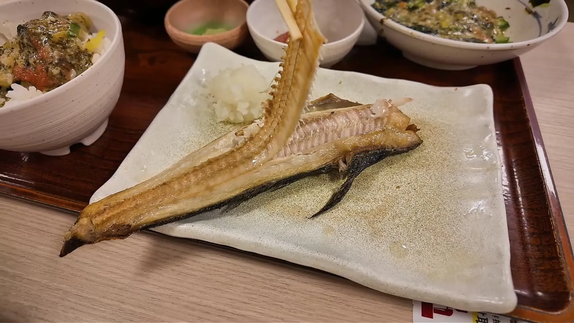 Chopsticks lifting the whole backbone out of a grilled shima hokke fish at Yayoiken, Tokyo.