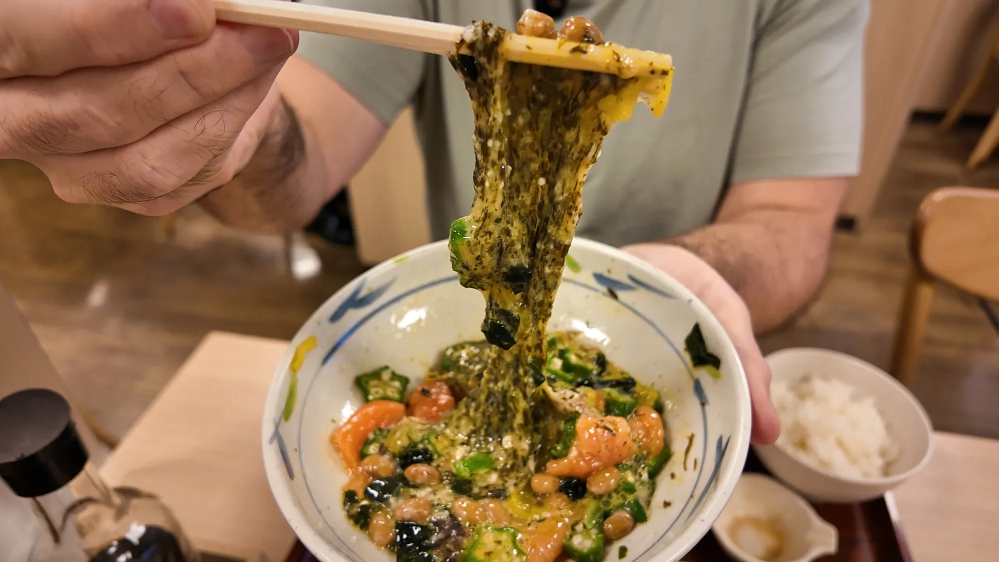 Chopsticks pulling long sticky strands of akamoku seaweed and natto out of a mixed Neba Toro bowl at Yayoiken.