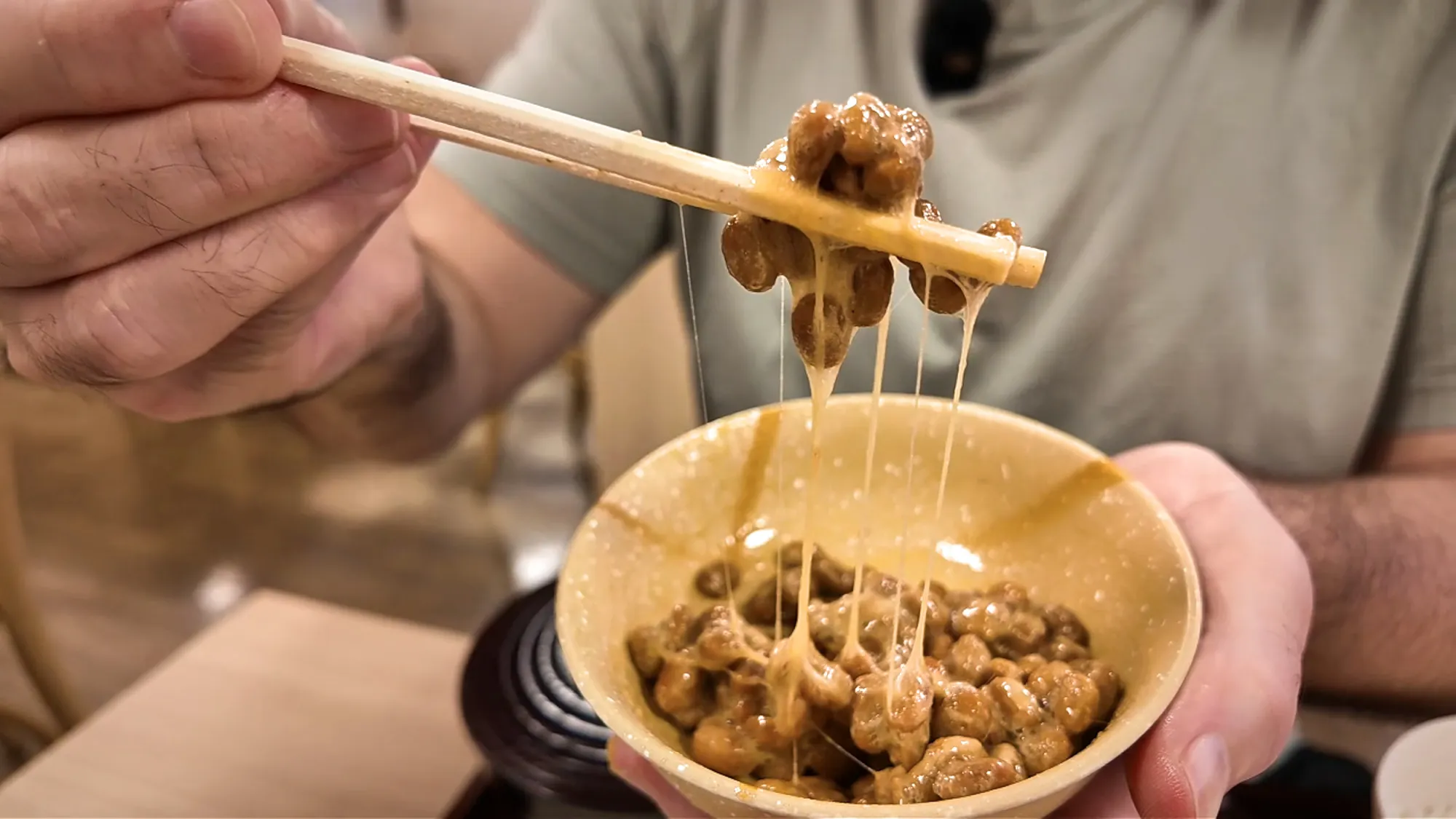 Chopsticks lifting stringy fermented natto soybeans out of a small bowl at Yayoiken in Tokyo.