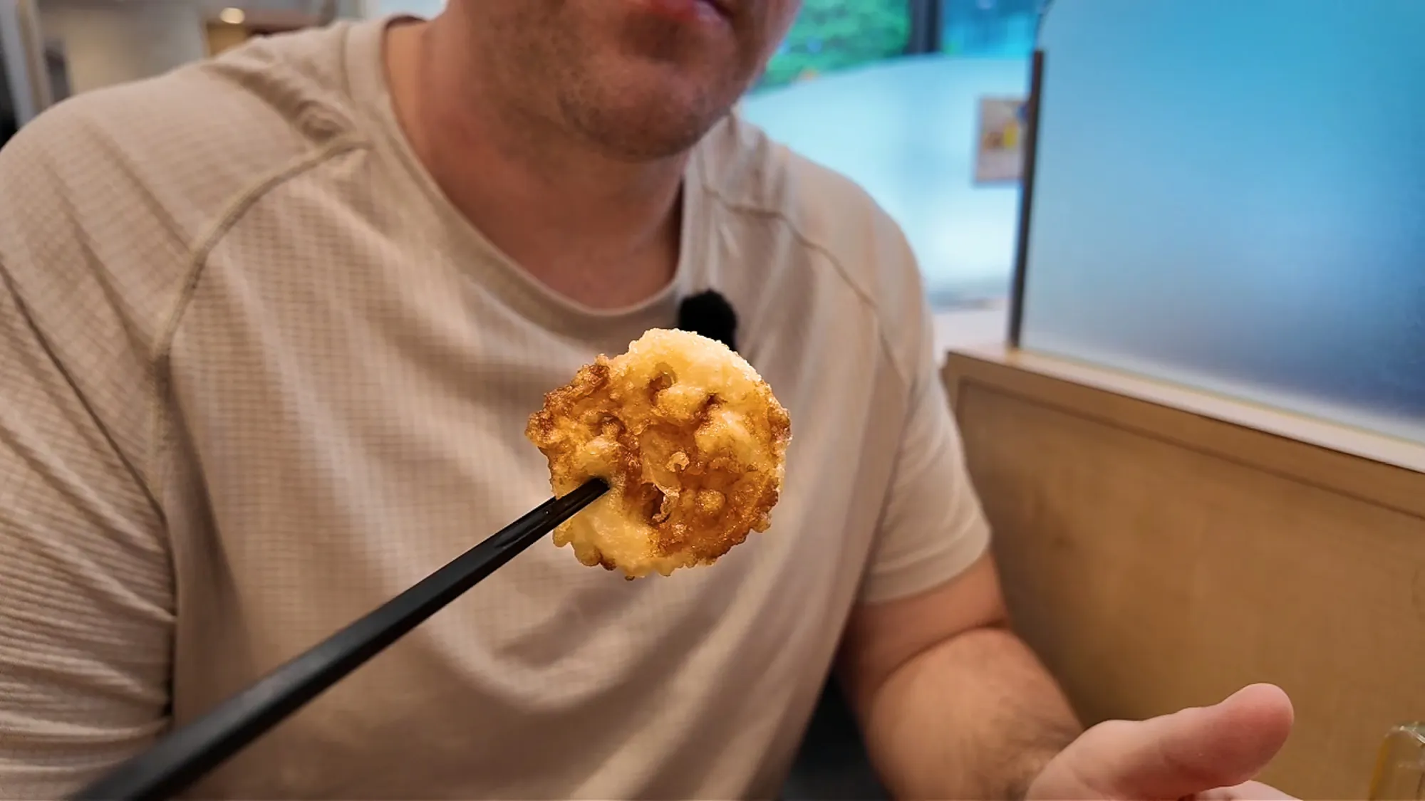 A round slice of lotus root tempura held up with chopsticks at Tendon Tenya in Tokyo.