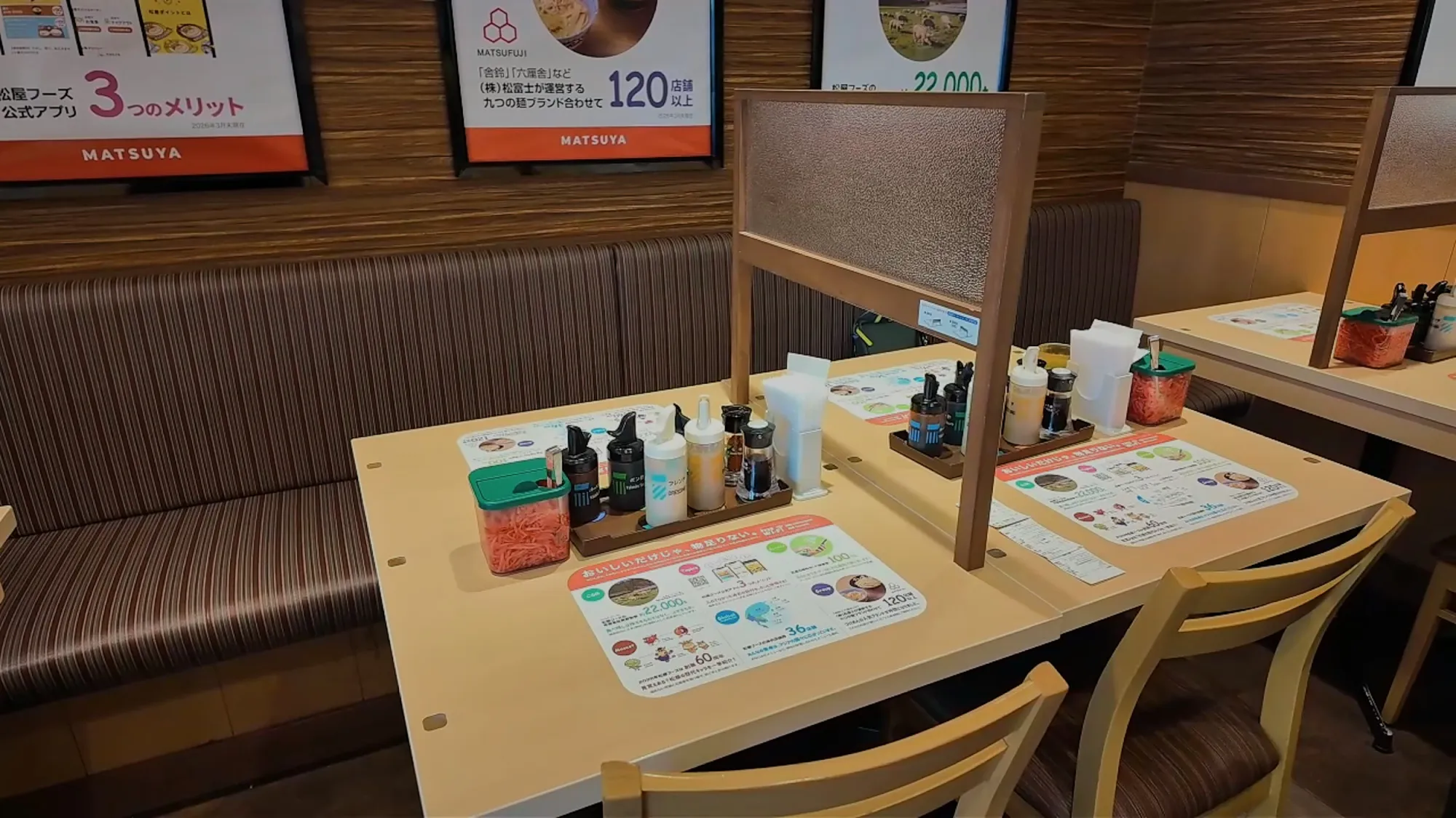 An empty booth table at Matsuya in Tokyo with frosted privacy dividers, sauce bottles, and a pickled ginger container.