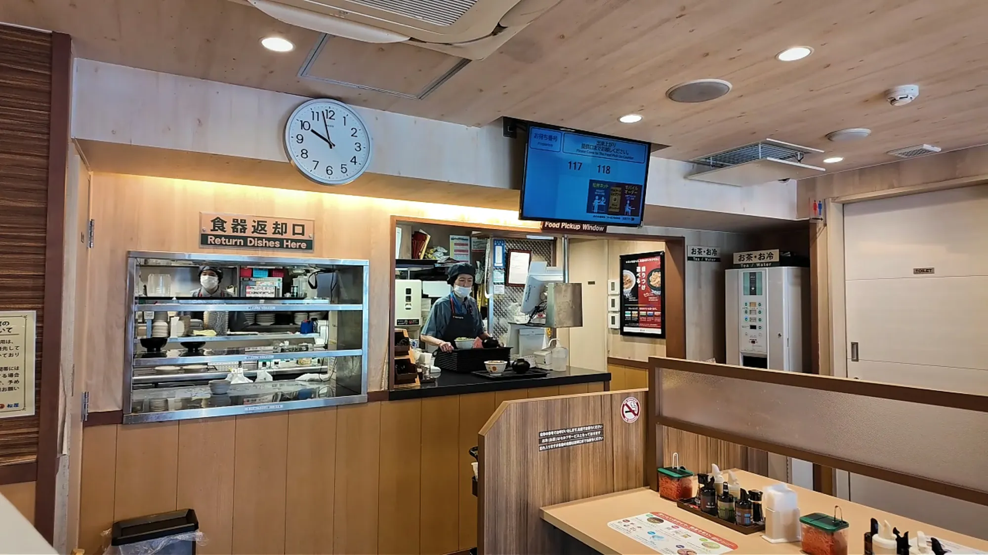 The counter and food pickup window inside a Matsuya in Tokyo, with an order number screen on the wall above.