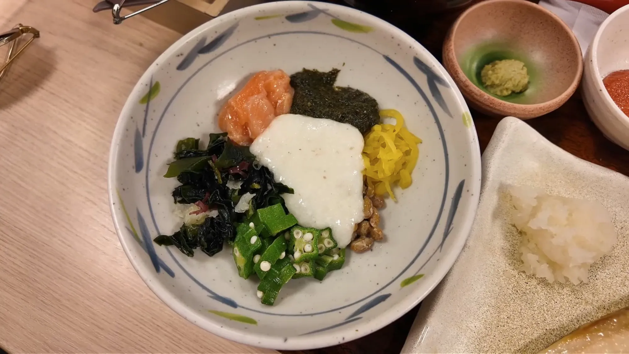 An Akamoku Neba Toro bowl at Yayoiken before mixing, with salmon, dark akamoku seaweed, grated yam, yellow pickled daikon, natto, okra, and wakame.