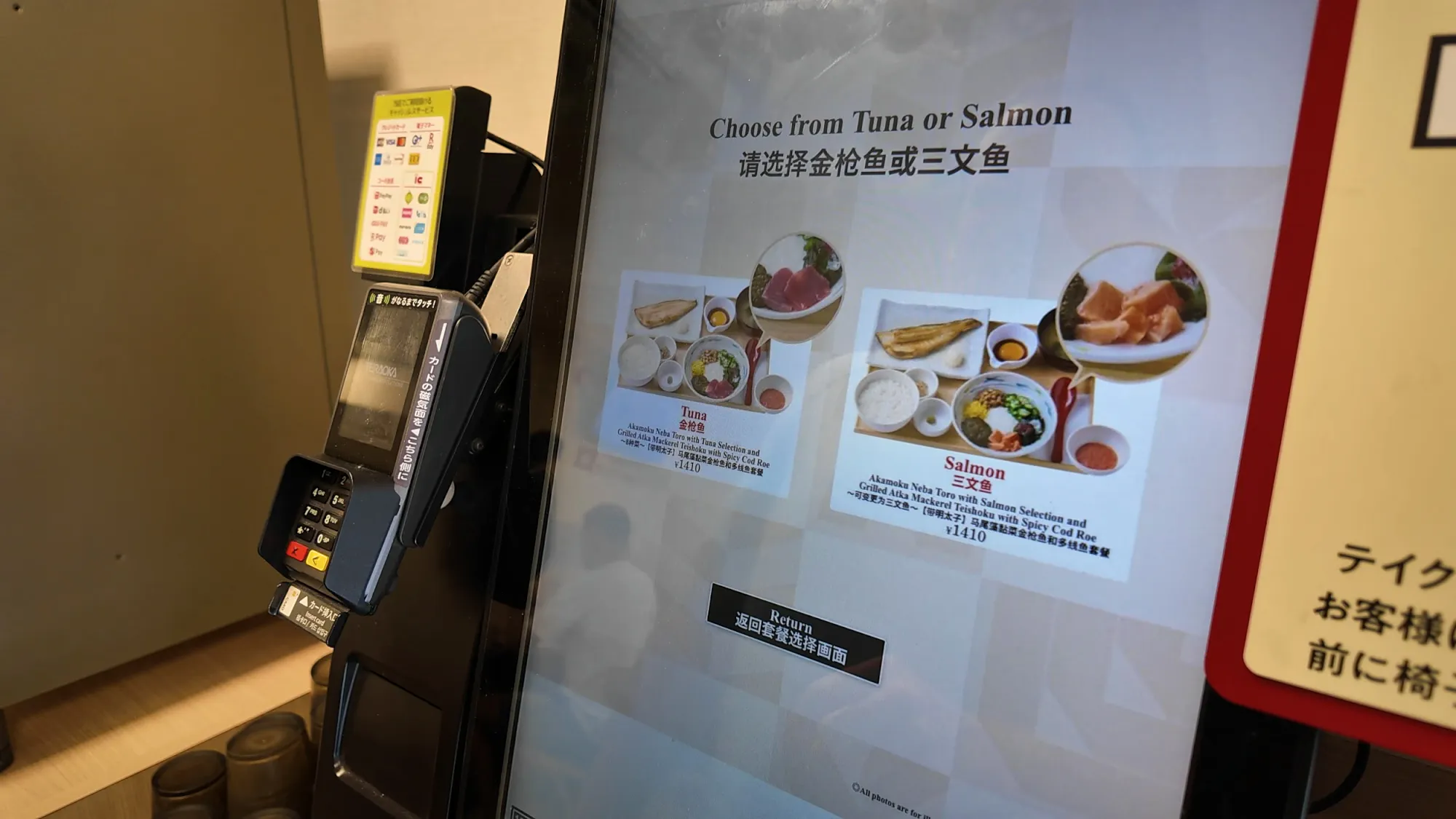 A Yayoiken ordering kiosk in Tokyo with an English screen asking to choose tuna or salmon for the Akamoku Neba Toro and grilled atka mackerel set, priced at 1,410 yen, next to a card reader.