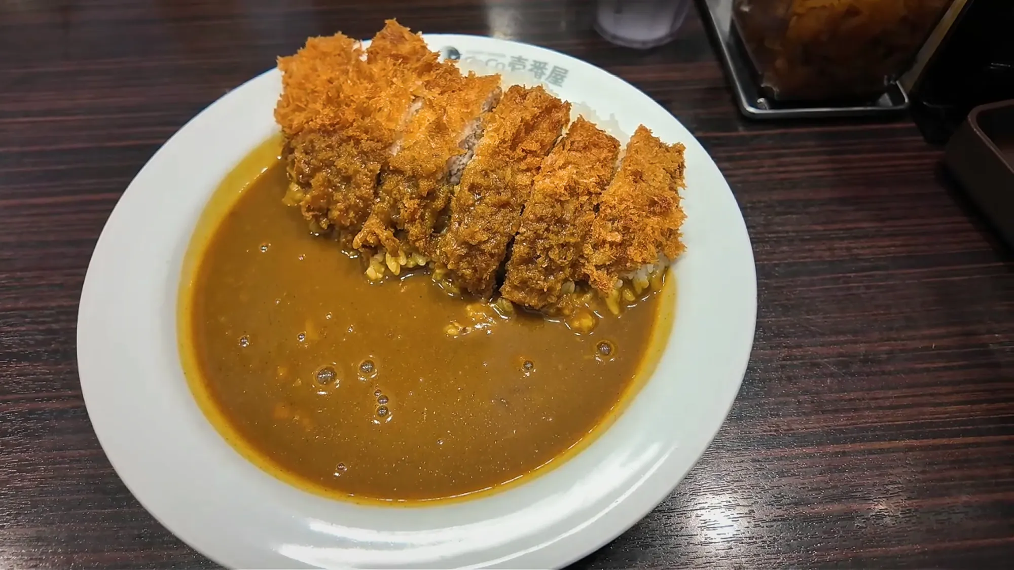 A crispy pork cutlet on a plate of thick brown Japanese curry and rice at CoCo Ichibanya