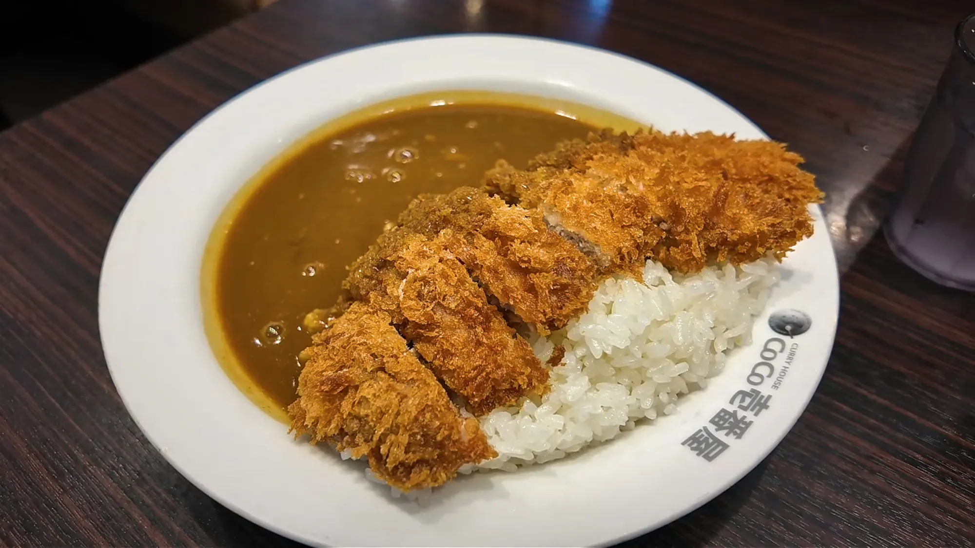 A white CoCo Ichibanya plate of pork cutlet curry, with the crispy sliced tonkatsu laid over white rice next to thick Japanese curry sauce, in Tokyo.