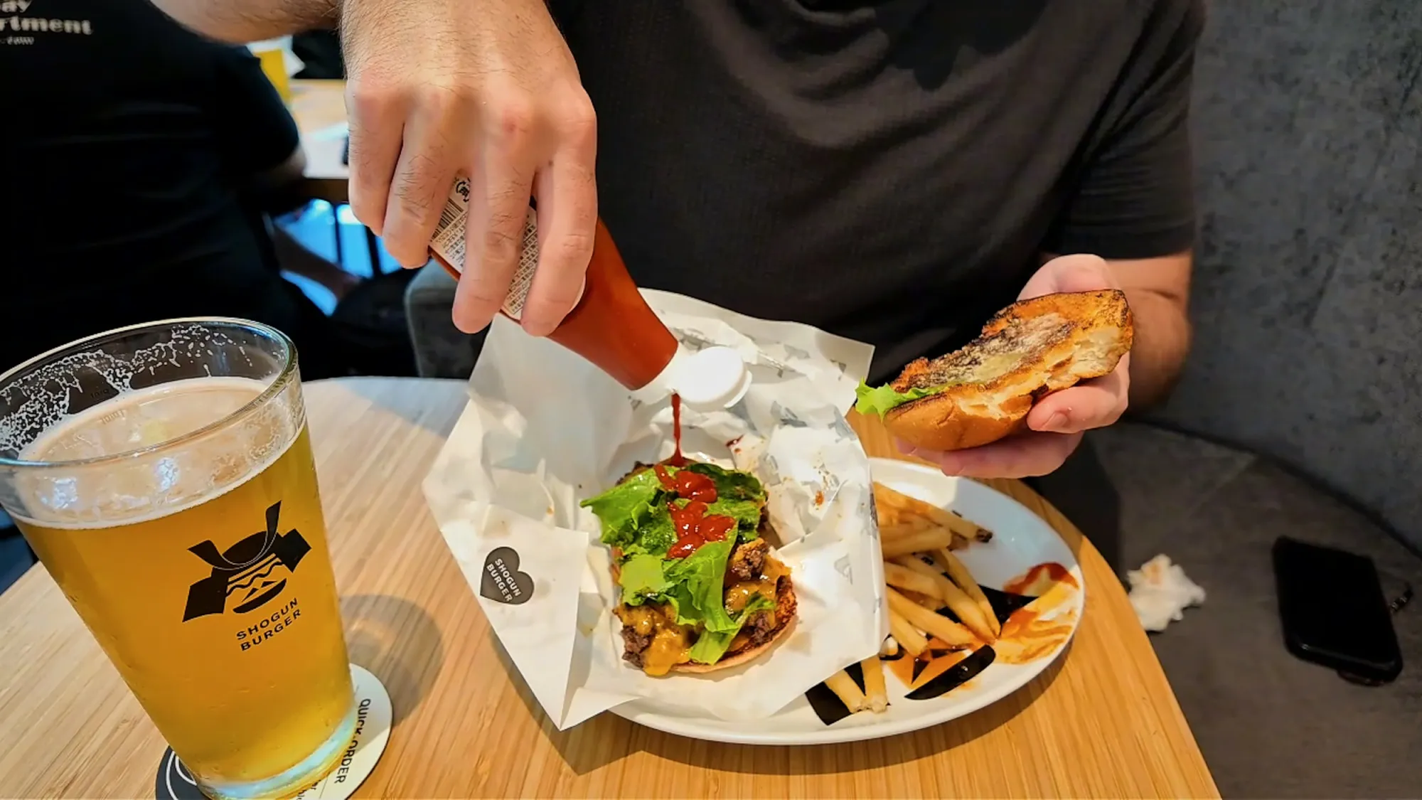 Squeezing a red table sauce onto a double cheeseburger, with a glass of Shogun draft beer beside the plate at Shogun Burger in Tokyo.