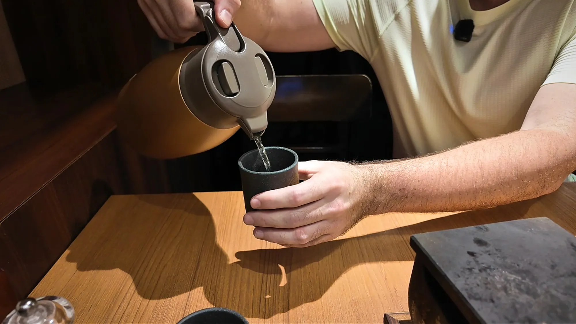 Pouring water from a jug into a small cup at a wooden restaurant counter in Tokyo.