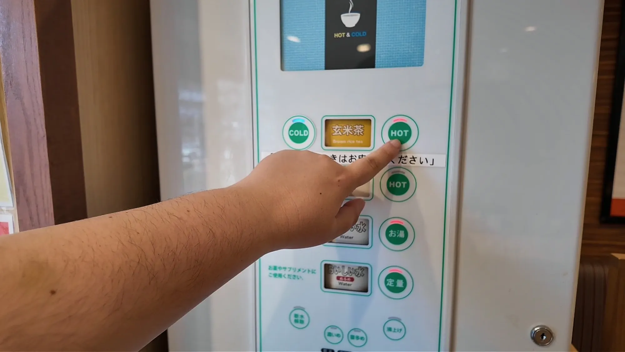 A hand pressing a button on a self-serve green tea machine in a Tokyo restaurant.