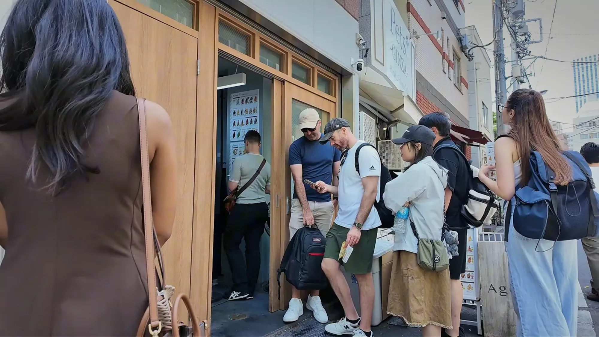 People crowded at the front of the line by the doors of the Age.3 shop in Ginza, with the menu board beside them.