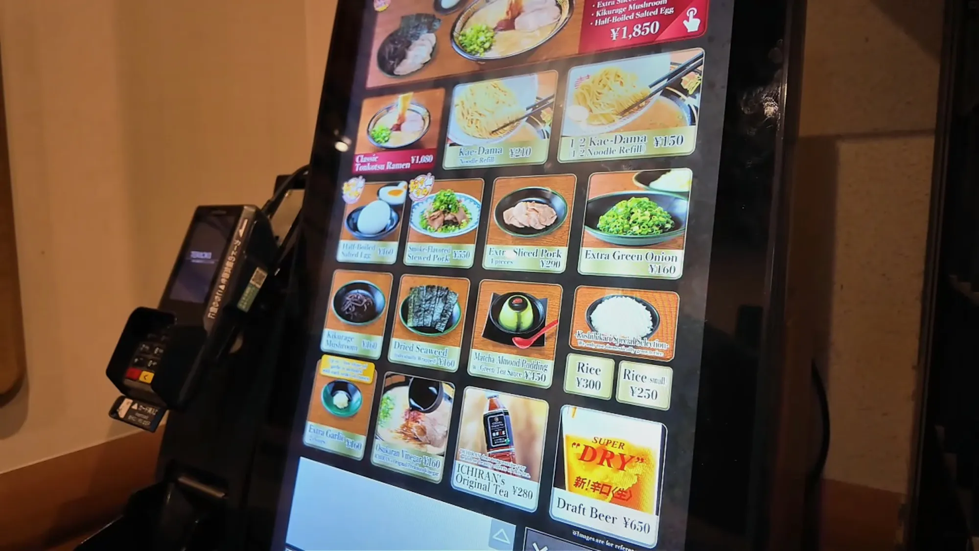The Ichiran touchscreen kiosk menu with ramen sets, toppings, rice, and a Super Dry draft beer button, beside the card reader.