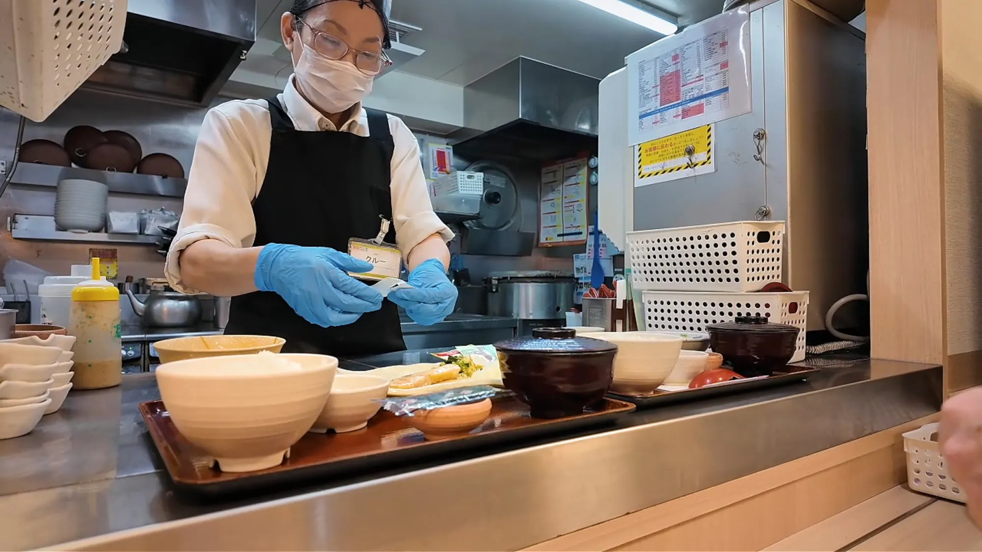 A cook in gloves and a mask putting breakfast trays together in the Yayoiken kitchen
