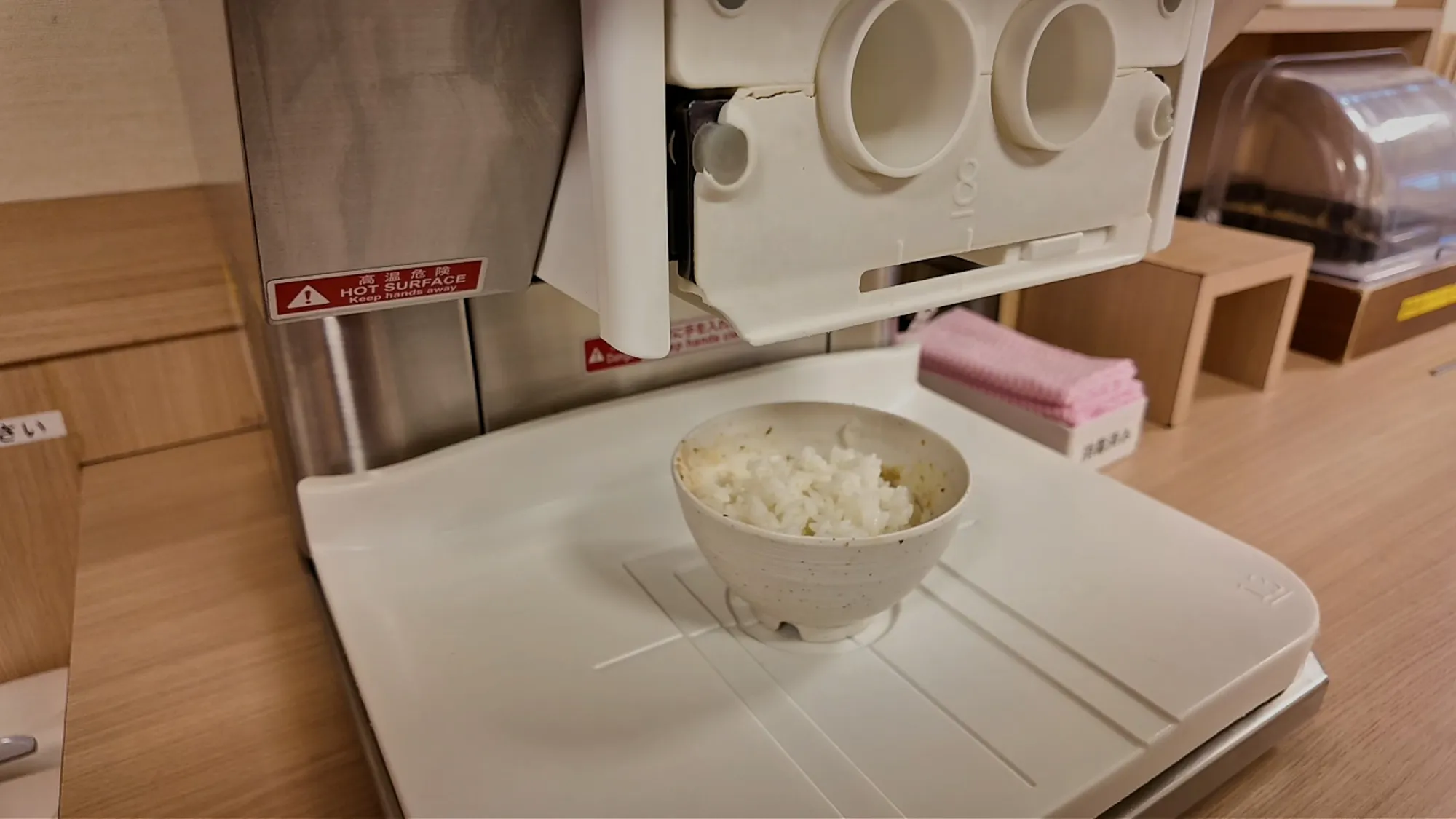 A bowl freshly refilled with white rice sitting under the rice refill machine at Yayoiken.