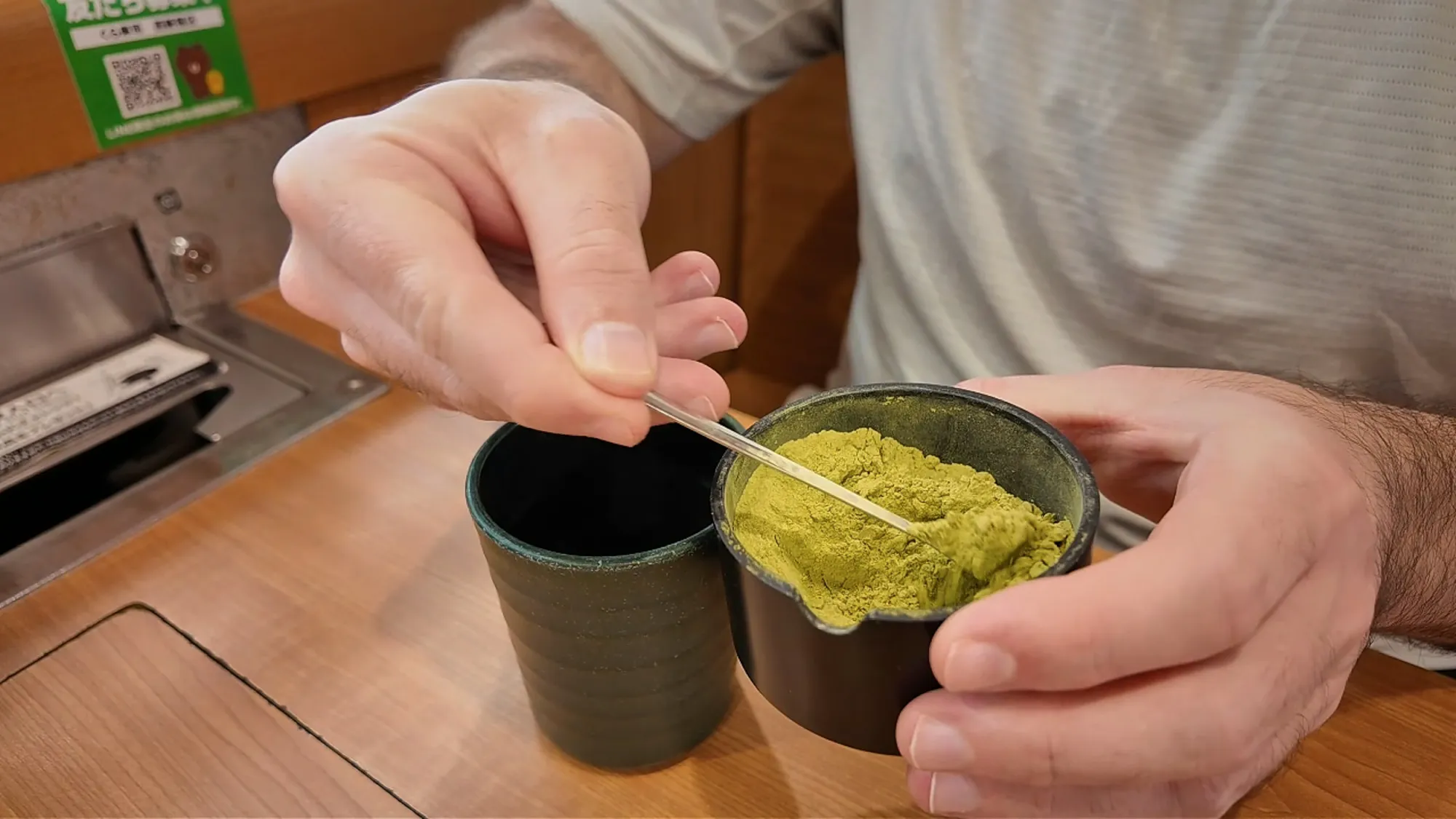 Cream scooping green tea powder into a cup at the table at Sushiro in Tokyo, before adding hot water from the tap.