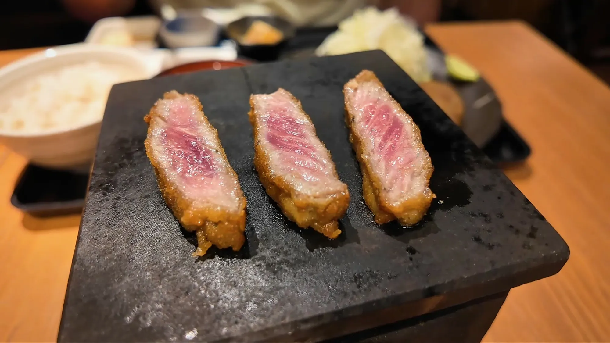 A slice of gyukatsu beef cutlet searing on a small hot stone grill at Gyukatsu Motomura in Shinjuku.