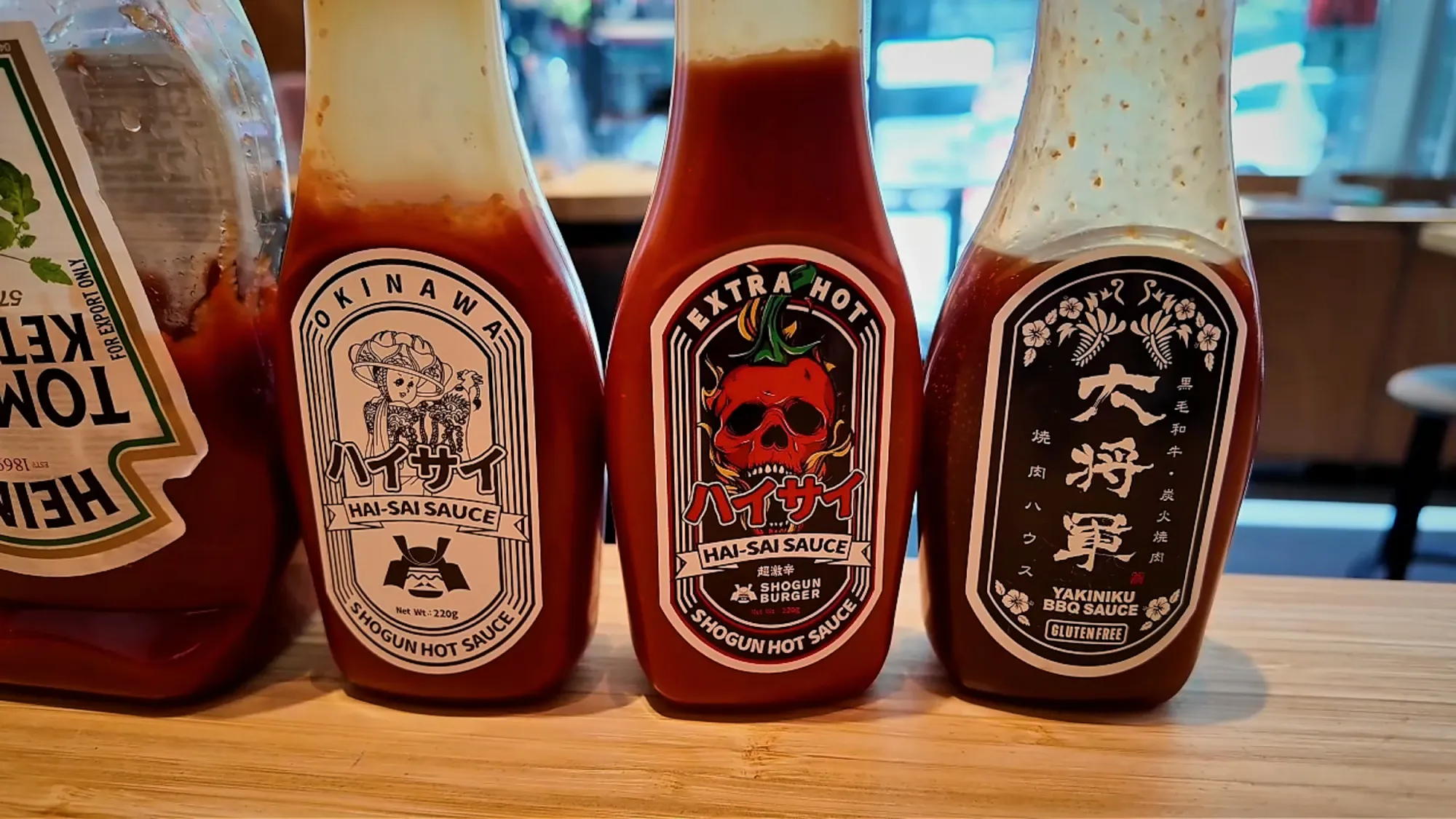 Bottles of Hai-Sai sauce, extra-hot Hai-Sai sauce, and Daishogun yakiniku barbecue sauce lined up on a wooden counter at Shogun Burger in Tokyo.