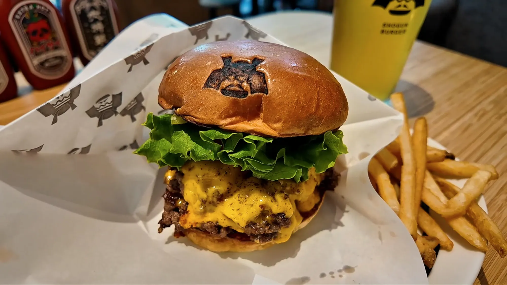 A Shogun Burger double cheeseburger with the samurai helmet logo branded on the bun, melted cheddar, and lettuce, served with fries on a wooden table.