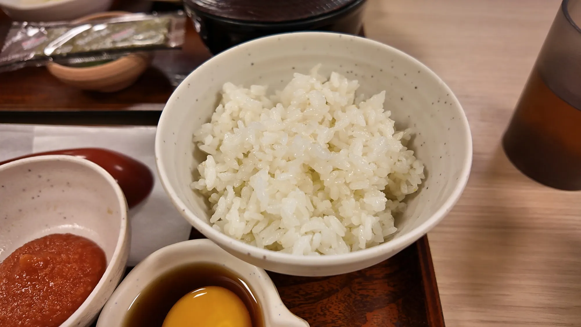 A bowl of white rice at Yayoiken next to a dish of mentaiko and a raw egg yolk in soy sauce.