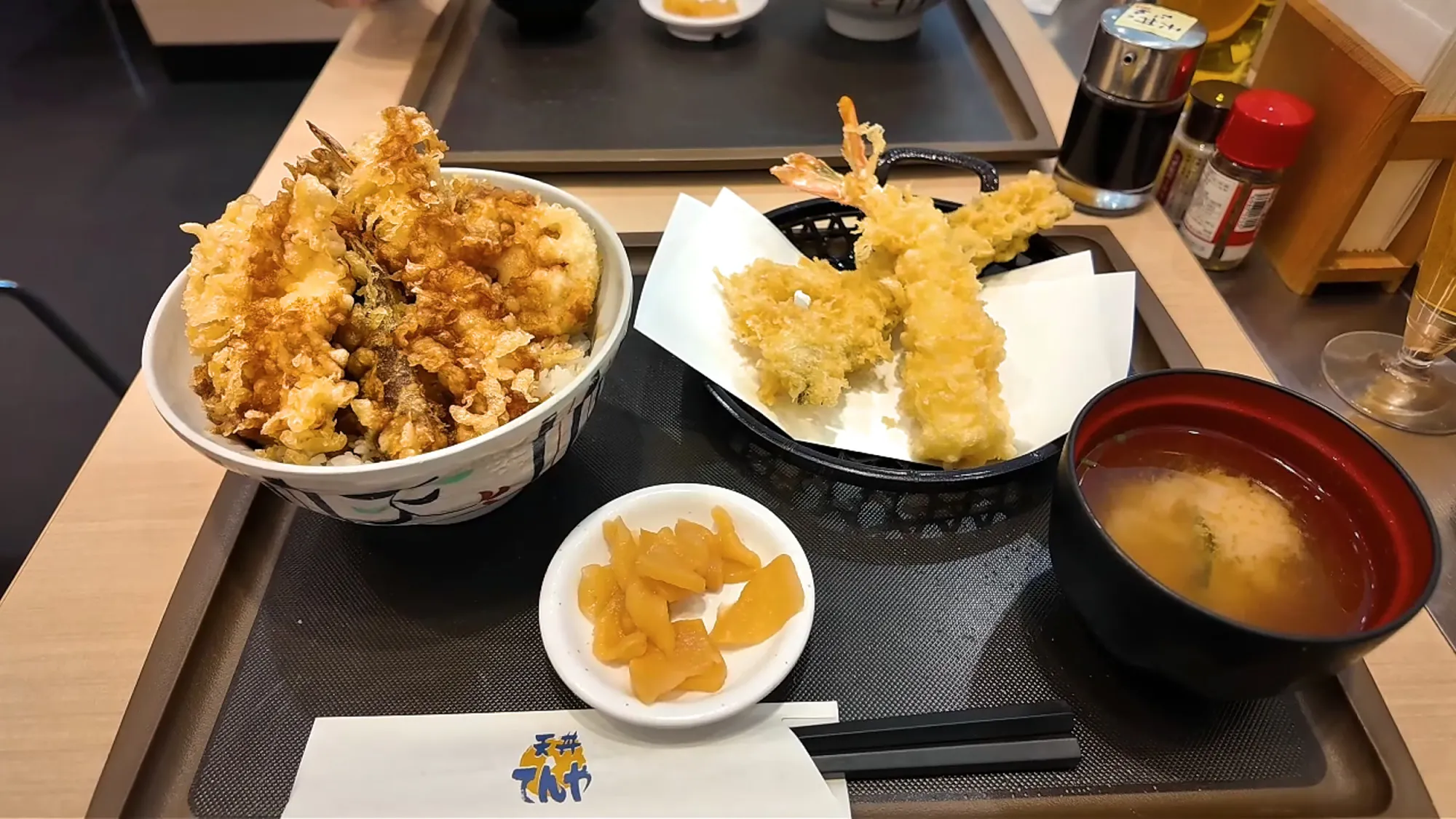 A tray at Tendon Tenya in Tokyo with an All-Star Tendon tempura bowl, a basket of large shrimp tempura, miso soup, and yellow pickles.