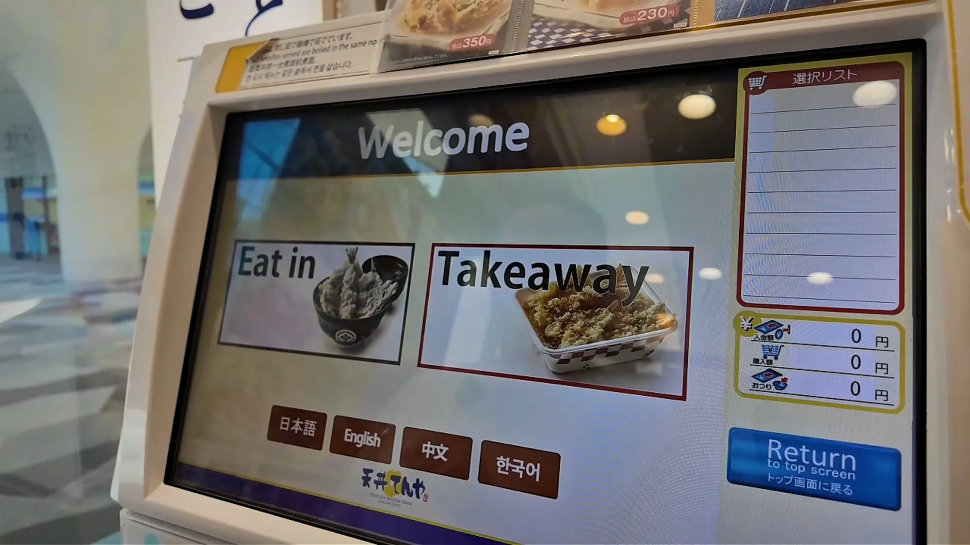 The Tendon Tenya ordering kiosk in Tokyo with its English welcome screen and eat-in and takeaway buttons.