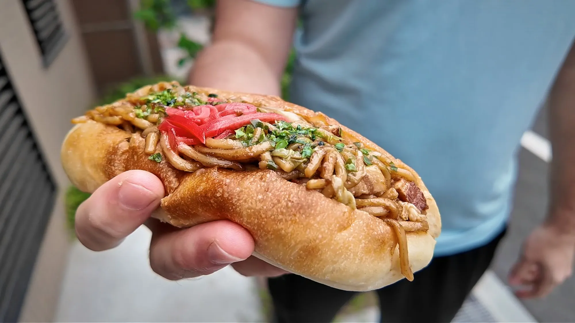 A yakisoba pan, a soft roll stuffed with fried noodles and red pickled ginger, held in a hand