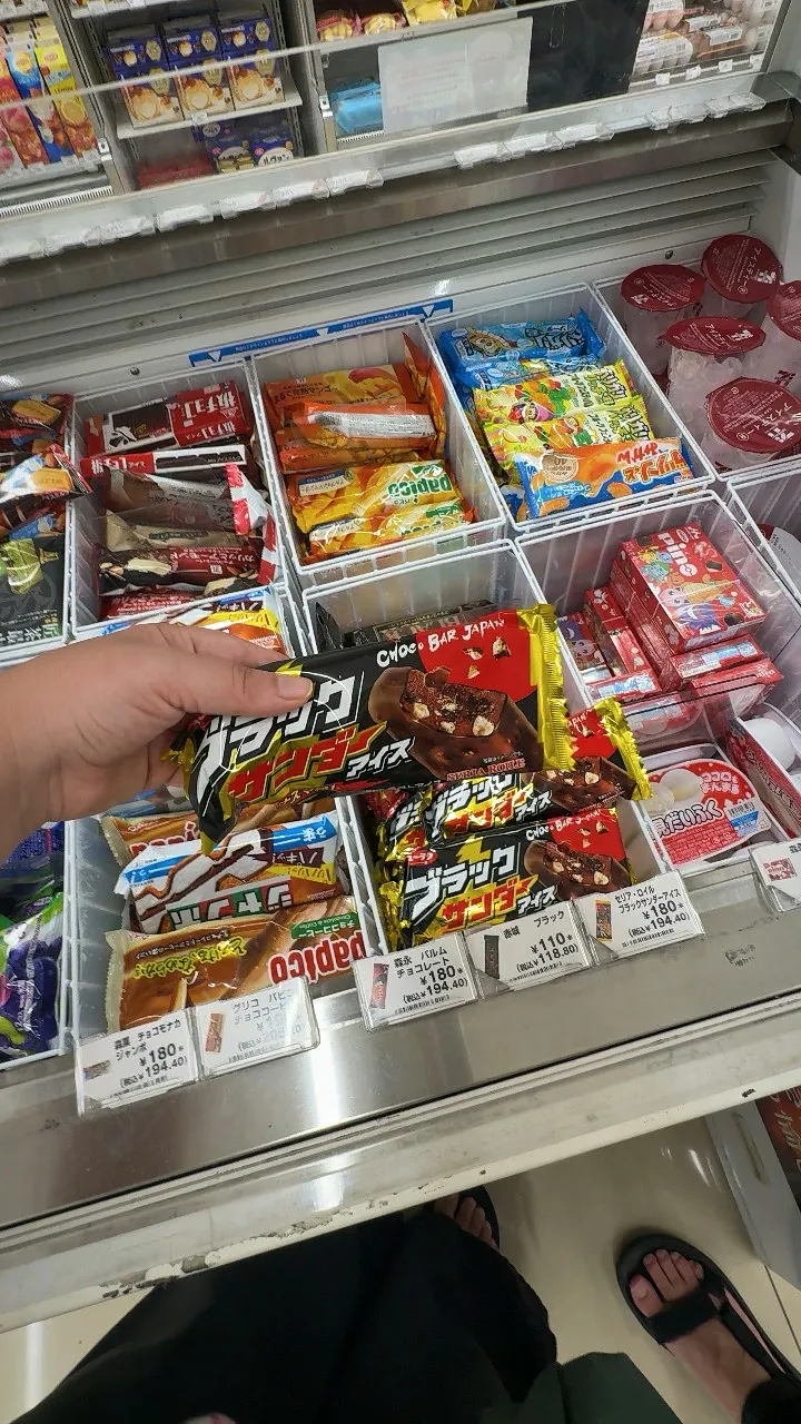 A hand holding a Black Thunder Ice chocolate bar above a 7-Eleven freezer in Tokyo, next to the 110 yen price tag.