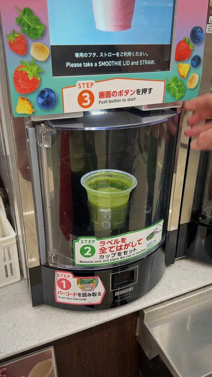 A green smoothie blended inside the clear door of the 7-Eleven smoothie machine, under a Step 3 push button sign.
