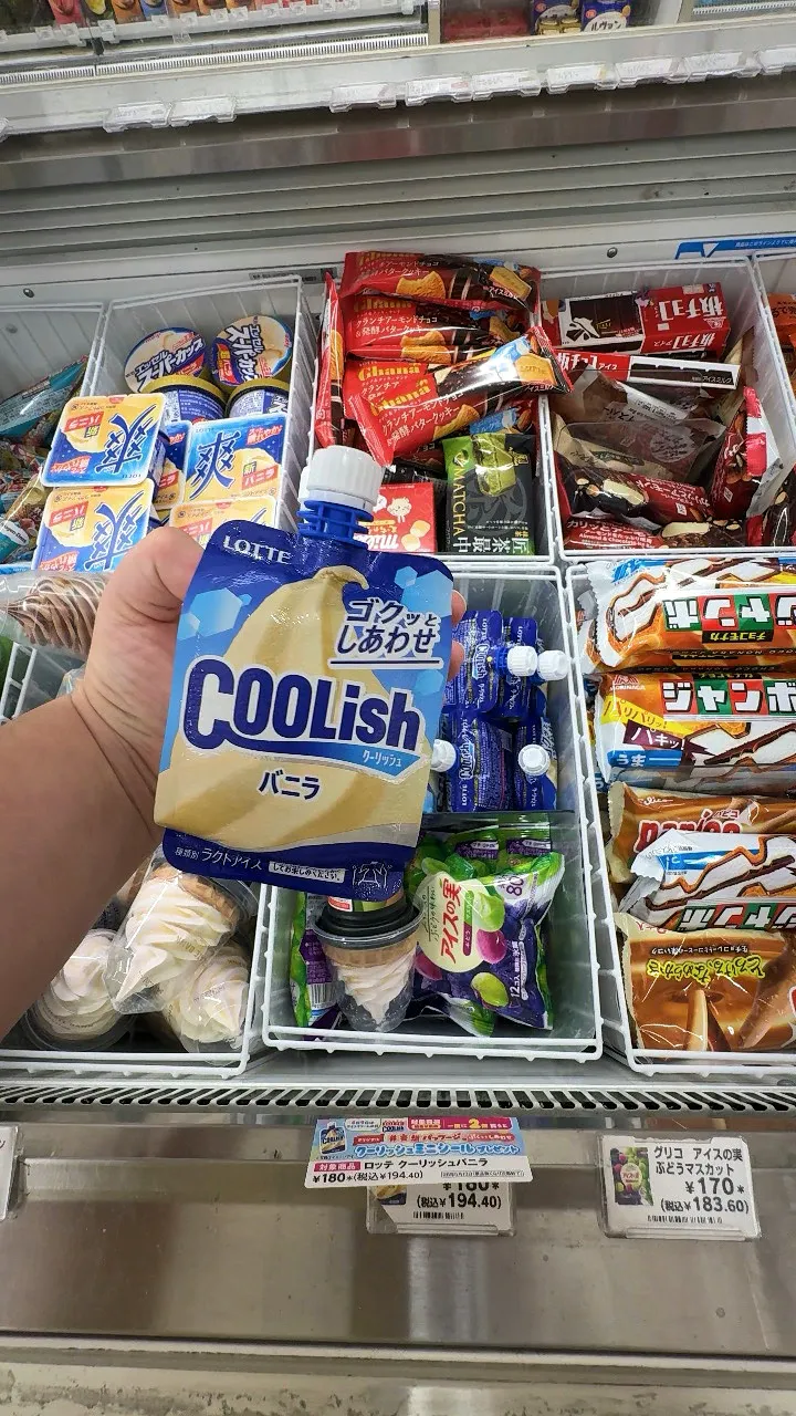 A hand holding a Lotte Coolish vanilla soft serve pouch above a 7-Eleven freezer in Tokyo.