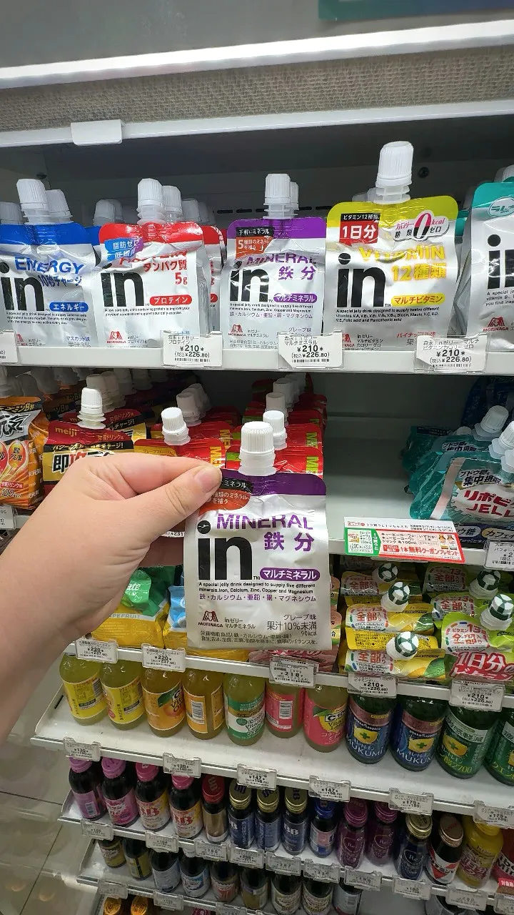 A hand holding a purple Morinaga in Jelly Multimineral pouch labeled iron below a row of in Jelly pouches at a 7-Eleven in Tokyo.