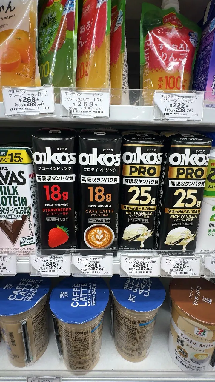 A 7-Eleven fridge shelf in Tokyo with oikos protein drinks labeled 18 g and 25 g of protein next to a SAVAS milk protein drink.