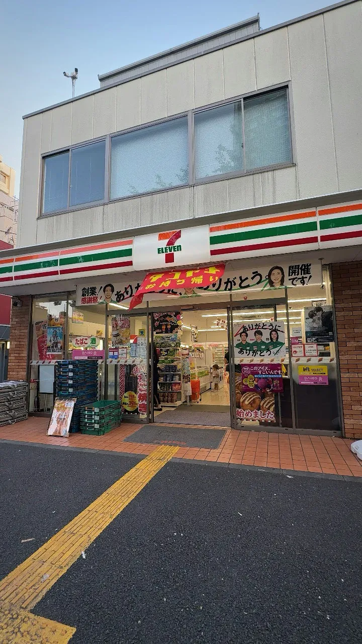 A 7-Eleven convenience store on a quiet street corner in Tokyo, with its orange, green, and red stripes over the entrance.