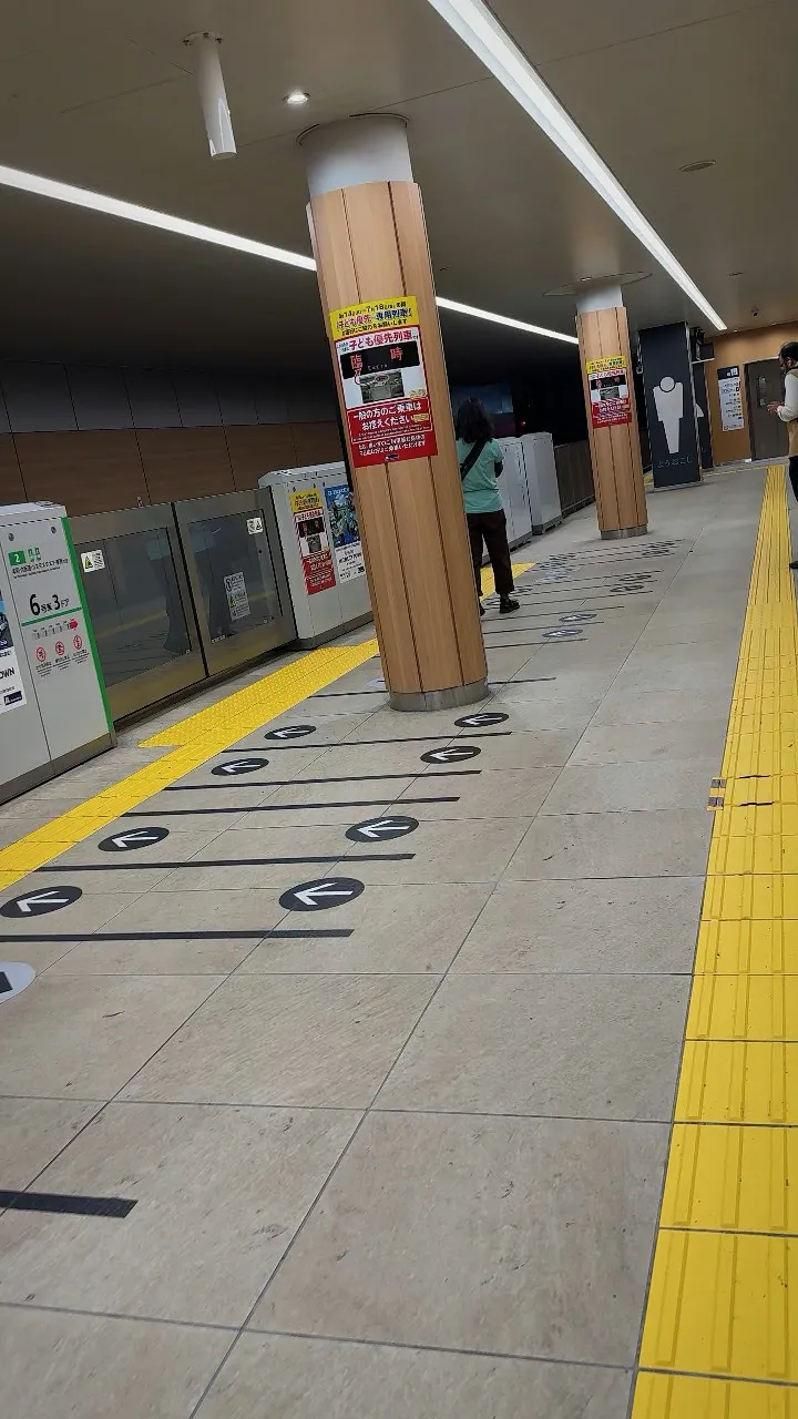 A long subway platform with black boarding lines and arrows on the floor beside the platform doors and a yellow tactile strip.