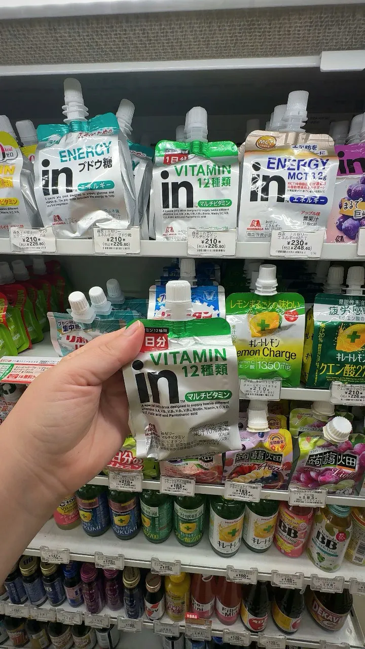 A hand holding a silver and green Morinaga in Jelly Multivitamin pouch labeled 12 vitamins in a 7-Eleven in Tokyo.