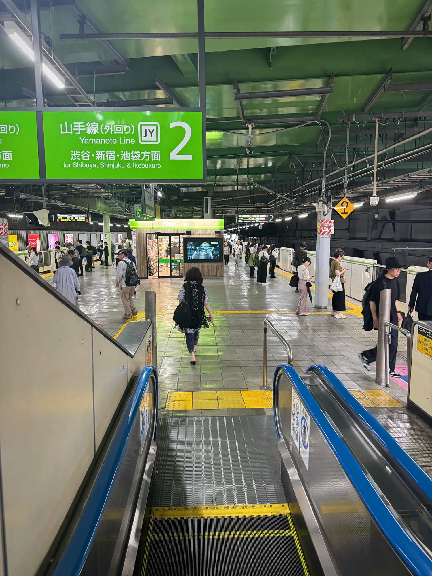 Looking down an escalator onto a JR Yamanote Line platform, under a green sign for platform 2 toward Shibuya, Shinjuku, and Ikebukuro.