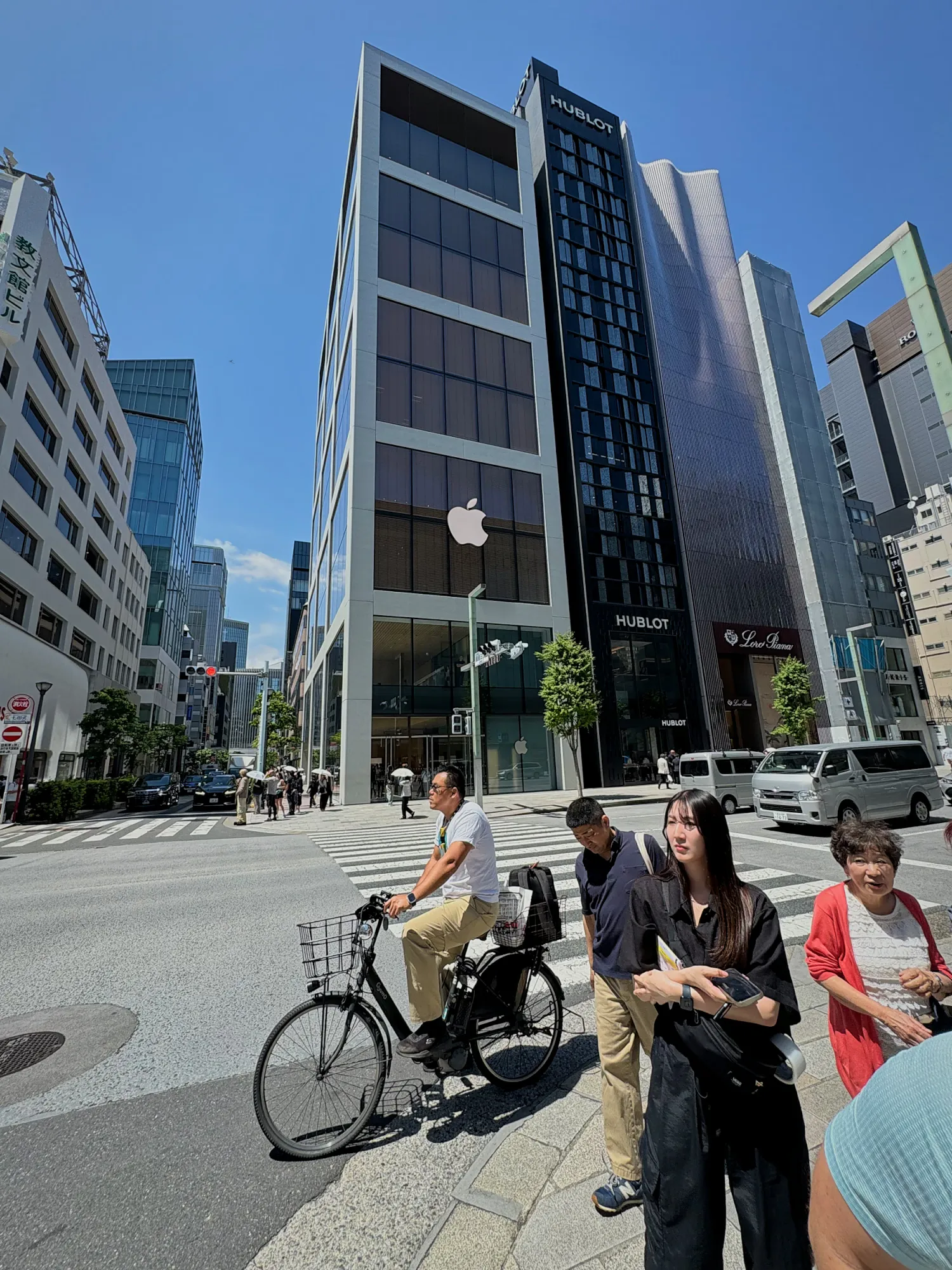People crossing a sunny street in front of the Apple store building in Ginza, Tokyo.